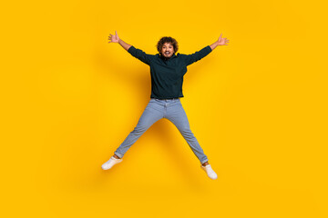 Joyful young man jumps against vibrant yellow background, dressed in casual black shirt and jeans