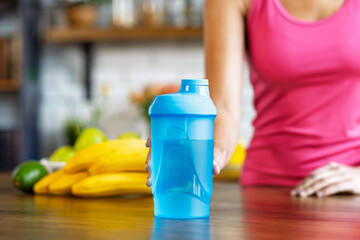 Woman holding a blue shaker bottle in a kitchen. Concept of healthy living, fitness, and nutrition