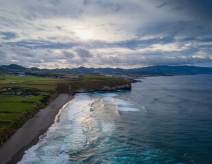 Obraz premium Santa Barbara beach with volcanic sand and turquoise Atlantic ocean waves in Sao Miguel, Azores. Aerial drone view of coast in Ribeira Grande town