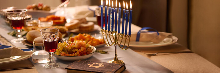 Website banner with lit blue candles and Torah with star of David on festive table