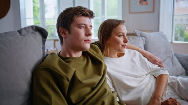 Happy lovers watching tv together on weekend. Teenager couple embracing on sofa