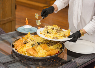 waiter puts pilaf on the plates of the guests
