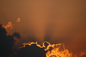 The sun hid behind a cloud. The sun bowed low to the horizon and hid behind a small cloud. The luminary illuminates the edges of the cloud and its rays spread across the sky in orange shades.