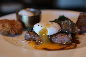 yolk flows from protein grill meat steak medium with egg soft-boiled egg Poached egg on a piece of bread with green lettuce leaves on a plate rotates, close up, breakfast concept