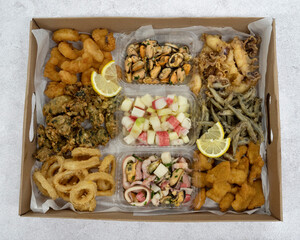 Seafood antipasti. Top view of a large box with different dishes such as fried squid rings and shrimps, fritters, squid and mussels with provencal, fish nuggets and salads	
