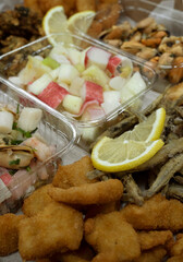 Seafood antipasti. Closeup view of plastic bowls with different dishes such as fried fish fritters, mussels with provencal and salads such as show salad with kani kama