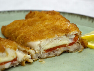 Mediterranean food. Closeup view of a sliced battered hake filet stuffed with melted mozzarella cheese and red bell pepper
