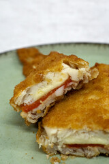 Mediterranean food. closeup view of a sliced battered hake filet stuffed with melted mozzarella cheese and red bell pepper