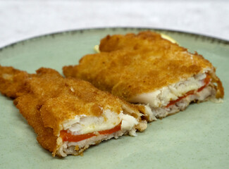 Mediterranean food. Closeup view of a sliced battered hake filet stuffed with melted mozzarella cheese and red bell pepper