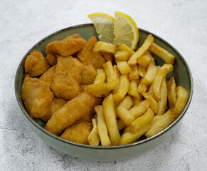 Seafood. Top view of a bowl with fried fish nuggets, lemon slices and potatoes with a white background