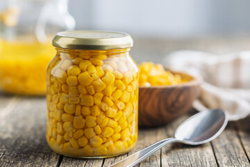 Canned sweet corn in jar on wooden table.