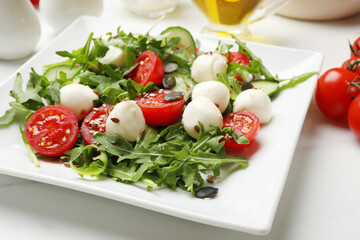 Tasty salad with arugula, mozzarella cheese and vegetables on white table, closeup