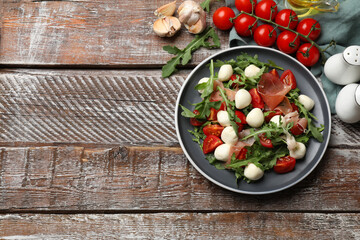 Tasty salad with arugula, mozzarella cheese, tomatoes and jamon on wooden table, flat lay. Space for text