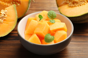 Pieces of Cantaloupe melon and mint in bowl on wooden table, closeup