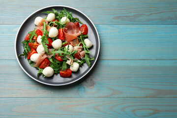Tasty salad with arugula, mozzarella cheese, tomatoes and jamon on light blue wooden table, top view. Space for text