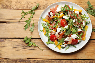 Tasty salad with arugula, cheese and vegetables on wooden table, flat lay. Space for text