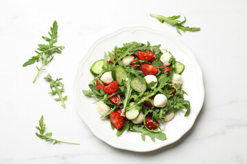 Tasty salad with arugula, mozzarella, tomatoes and cucumber on white marble table, flat lay