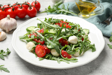 Tasty salad with arugula, mozzarella, tomatoes and cucumber on grey textured table, closeup