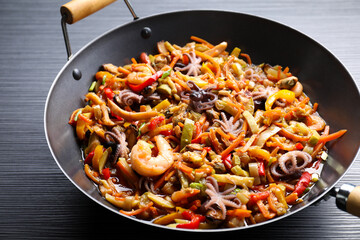 Stir-fry sea food in wok on black wooden table, closeup