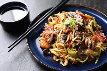 Stir-fry noodles with sea food, vegetables and soy sauce on dark textured table, closeup