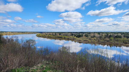 Panoramic view of river bend, forest and blue sky. Beautiful reflection of white clouds in water at sunny day. Aerial view of picturesque background. High quality photo