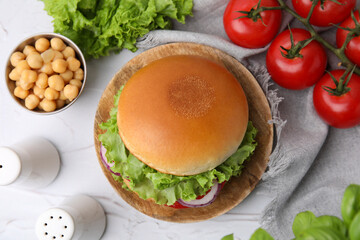 Delicious vegetarian burger with chickpea cutlet and ingredients on white textured table, flat lay