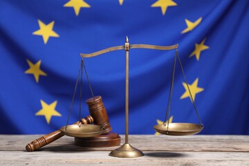 Scales of justice and judge's gavel on wooden table against European Union flag