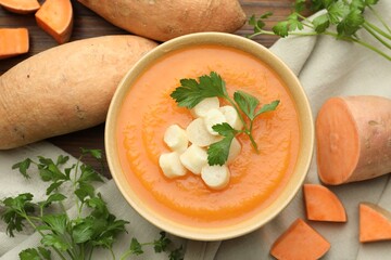 Delicious sweet potato soup with croutons in bowl, fresh vegetables and parsley on wooden table, flat lay