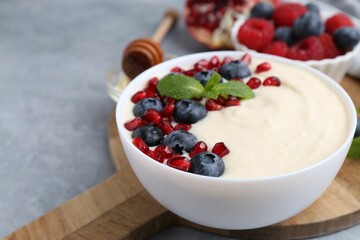 Tasty cooked semolina porridge with blueberries, pomegranate and mint on grey table, closeup