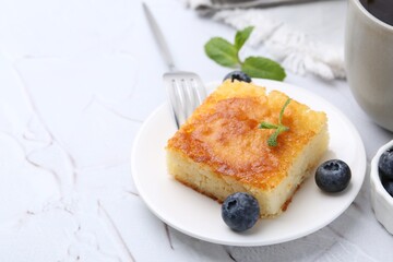 Slice of tasty semolina cake served on white textured table, closeup. Space for text