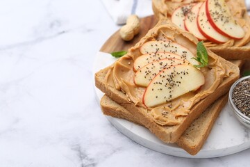 Tasty sandwiches with peanut butter, apple, chia seeds and mint on white marble table, closeup. Space for text