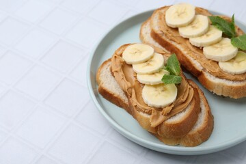 Tasty sandwiches with peanut butter, banana and mint on white tiled table, closeup. Space for text