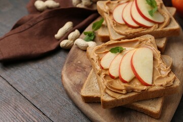 Tasty sandwiches with peanut butter, apple, nuts and mint on wooden table, closeup