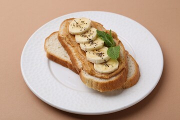 Tasty sandwich with peanut butter, banana, chia seeds and mint on brown background, closeup