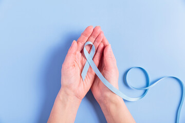 A blue cancer ribbon held by two female hands on a soft blue background. This image evokes support and hope for colorectal cancer patients and awareness initiatives.