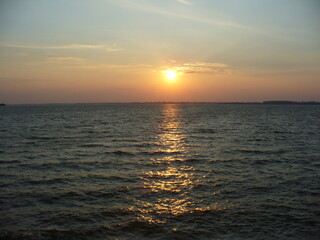 Blue sky with orange and yellow sunset over horizon of dark water surface with reflection of sunlight on water with small waves - natural evening scene. Topics: weather, natural environment, season