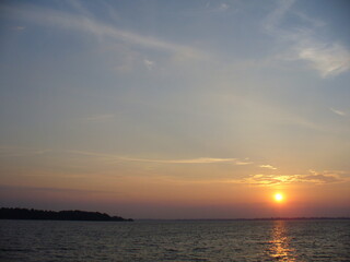 Obraz premium Blue sky with orange and yellow sunset over horizon of dark water surface with reflection of sunlight on water with small waves - natural evening scene. Topics: weather, natural environment, season