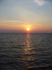 Blue sky with orange and yellow sunset over horizon of dark water surface with reflection of sunlight on water with small waves - natural evening scene.