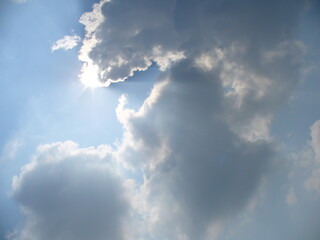 Natural blue and white sky background with sun rays coming out from behind clouds. Topics: weather,...