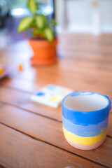 Hand painted mug on an art and craft wooden table with many tools and brushes