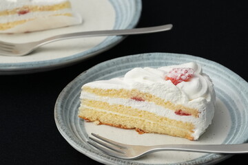 A small Japanese strawberry shortcake and a fork each on two stylish Japanese-style large and small plates on a black cloth on a white table
