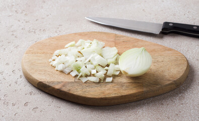 Wooden board with chopped onion and a knife on a beige stone table, top view