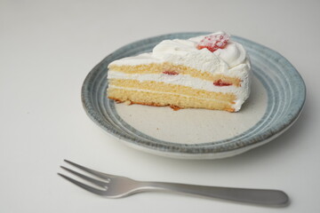 One small Japanese strawberry shortcake and a small fork on a stylish Japanese plate on a white table