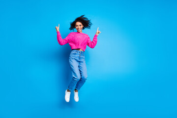 Full length photo of lovely young lady jump point up empty space dressed stylish pink garment isolated on blue color background
