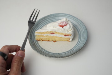 A small Japanese strawberry shortcake on a stylish Japanese plate on a white table and a man's hand holding a small fork to eat it.
