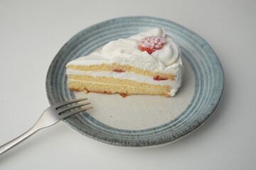 One small Japanese strawberry shortcake and a small fork on a stylish Japanese plate on a white table