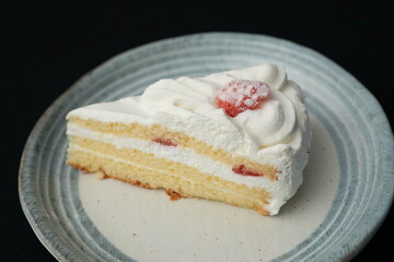 One small Japanese strawberry shortcake on a stylish Japanese plate on a black cloth on a white table