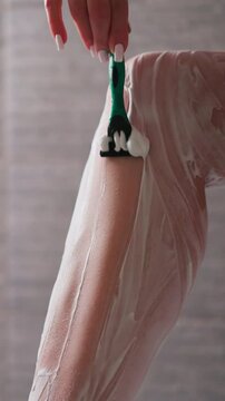 Woman shaves leg with foam and razor in shower closeup. Lady removes body hair from skin using mouse and blade in bathroom. Skincare and beauty nb