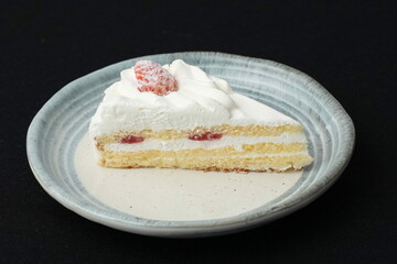 One small Japanese strawberry shortcake on a stylish Japanese plate on a black cloth on a white table