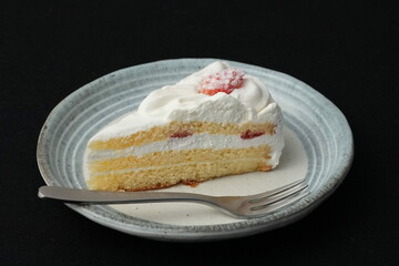 One small Japanese strawberry shortcake and a small fork on a stylish Japanese plate on a black cloth on a white table